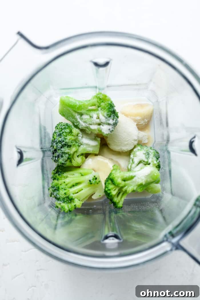 Frozen broccoli and other smoothie ingredients being added to a blender.