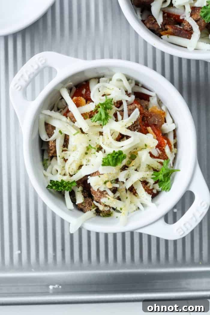 White dish filled with pizza bowl ingredients, topped with herbs and spices before baking.