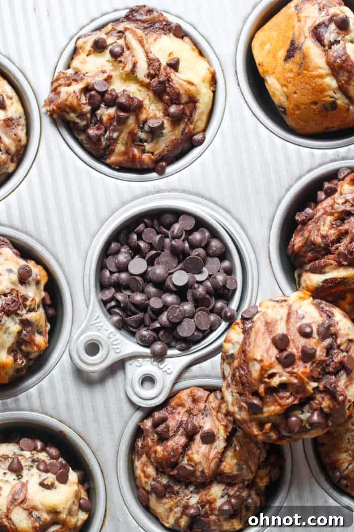 A muffin pan filled with unbaked gluten-free banana muffin batter, topped with mini chocolate chips.