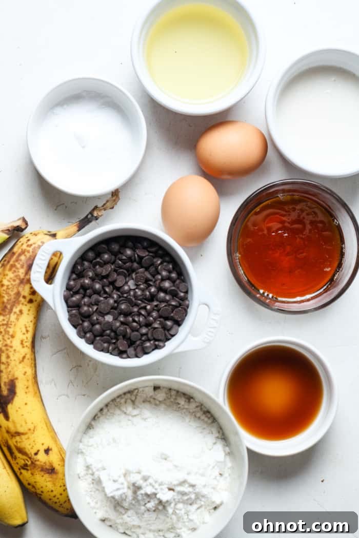 Bowls of coconut oil, maple syrup, mashed bananas, and other key dairy-free banana bread ingredients laid out on a kitchen counter.
