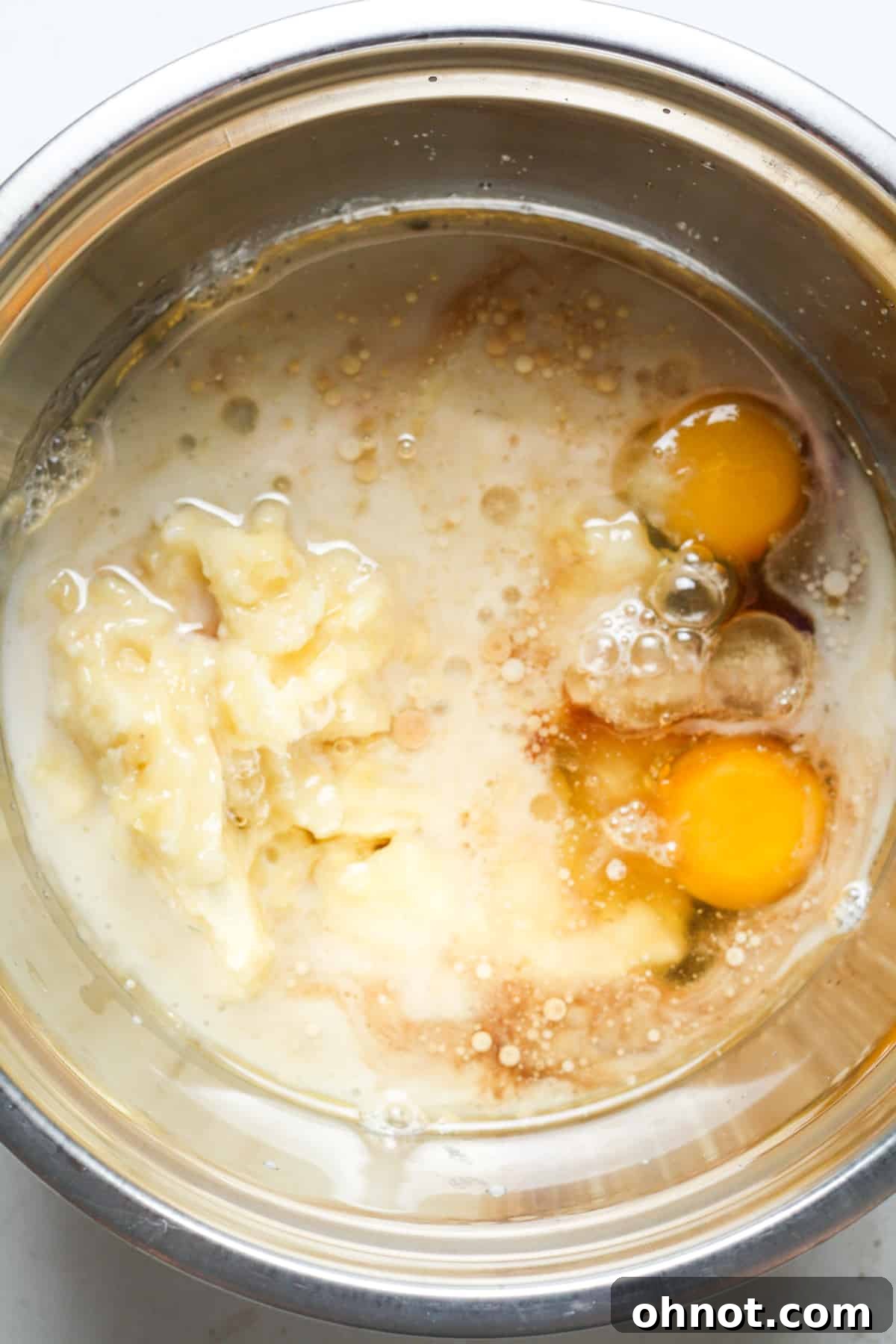Two eggs and mashed bananas ready to be mixed in a bowl with other wet ingredients.
