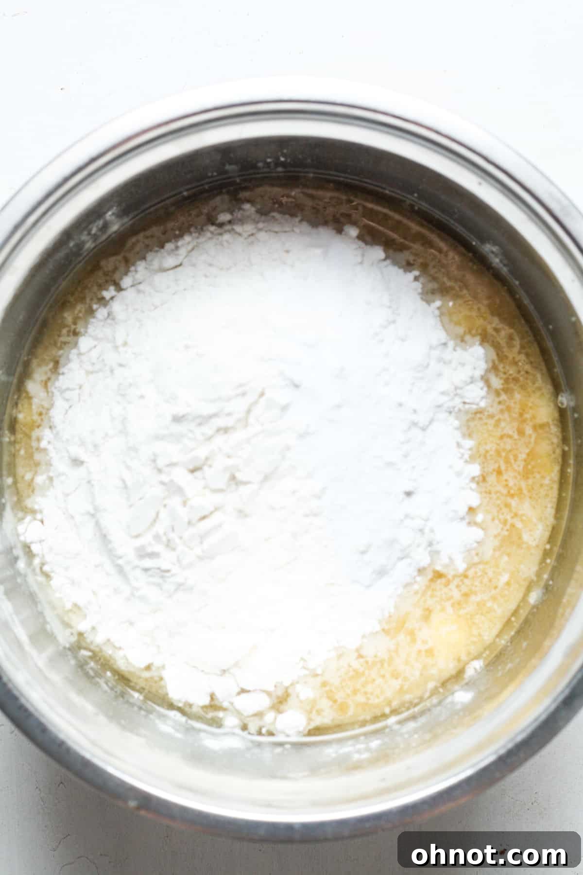 Gluten-free flour being added to the mashed banana and wet ingredient mixture in a bowl.