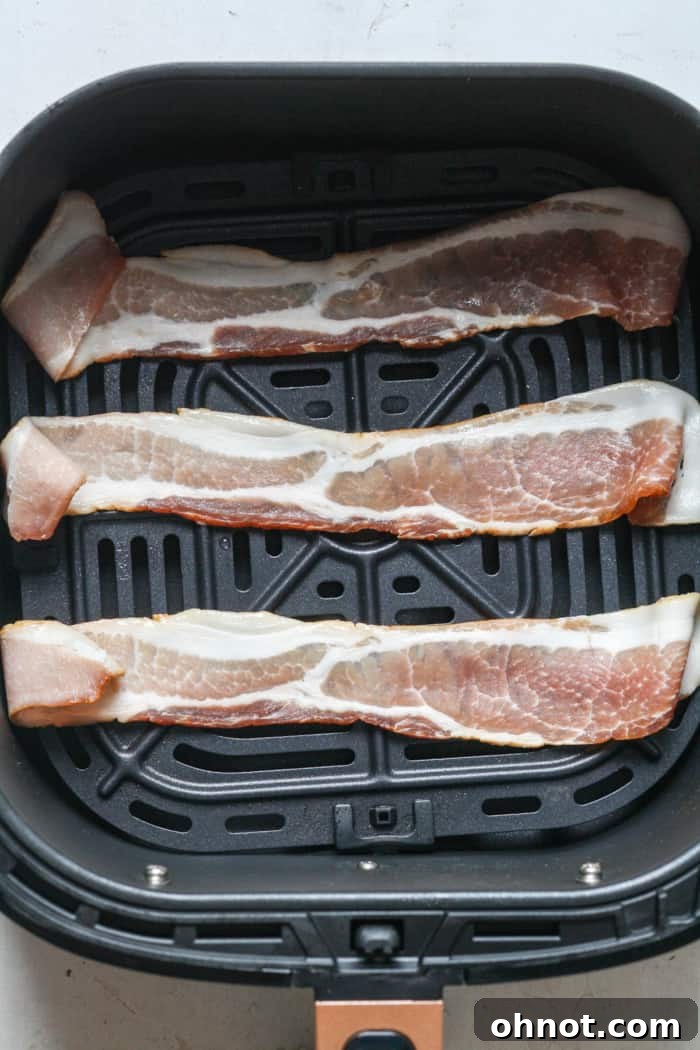 Raw bacon strips neatly arranged in an air fryer basket.