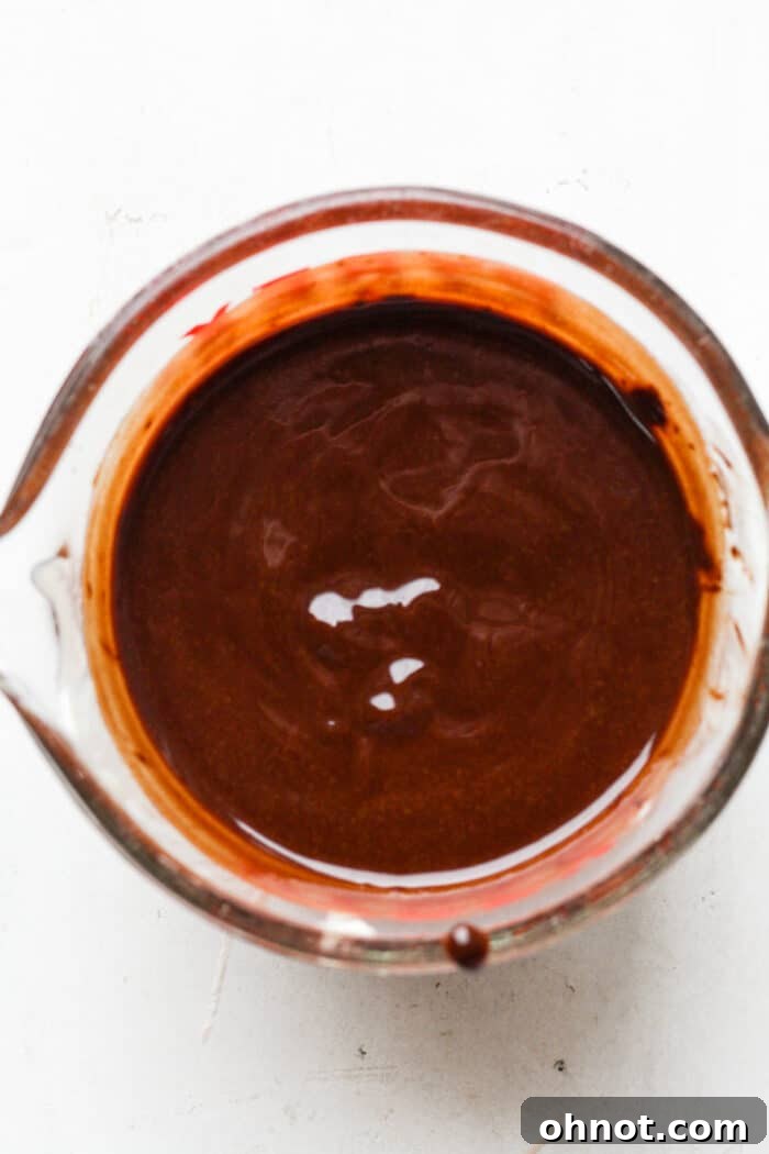 Smooth, melted dark chocolate and oil mixture in a bowl, forming the base of the brownies.