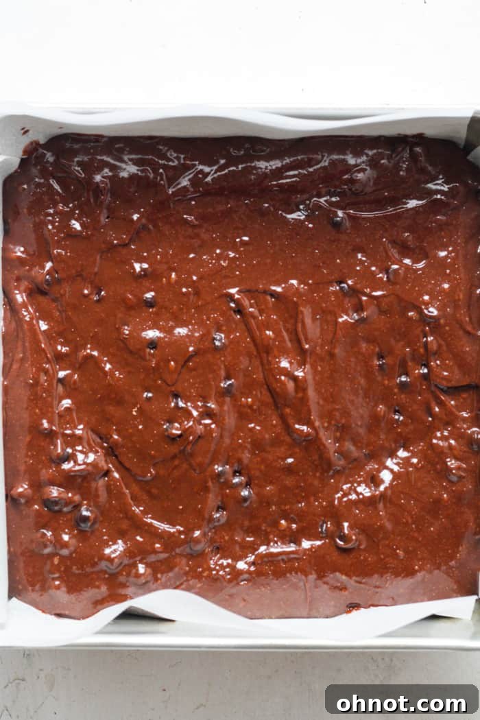 Brownie batter spread evenly in a square baking pan, filling it perfectly.