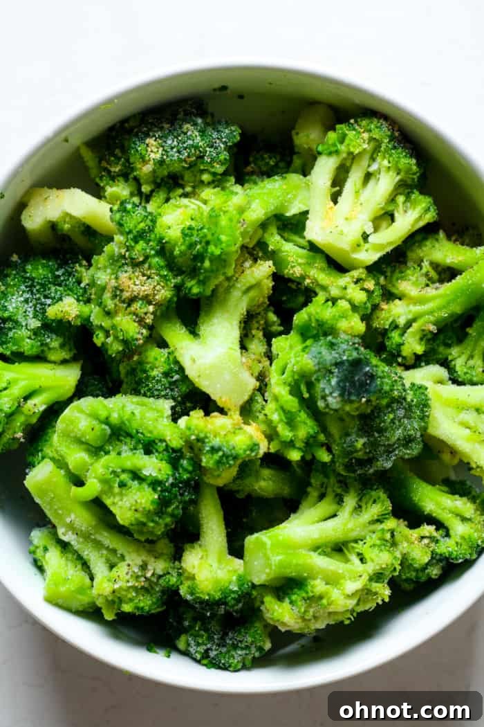Frozen broccoli florets being tossed with oil and seasonings in a mixing bowl.