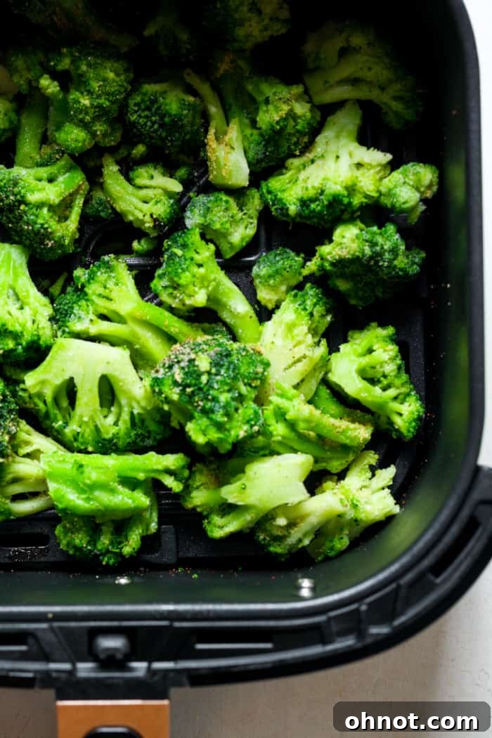 Seasoned frozen broccoli arranged in a single layer within an air fryer basket.