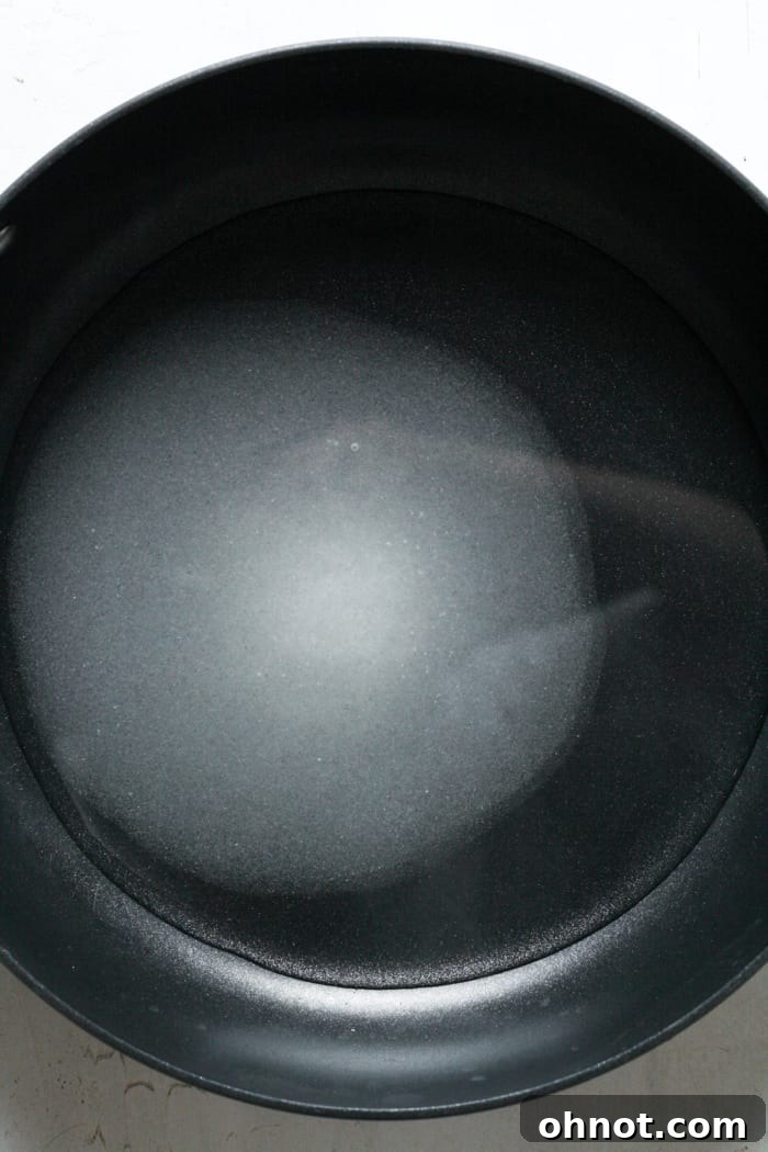 Granulated sugar being poured into a large skillet with water, ready to be heated for simple syrup.