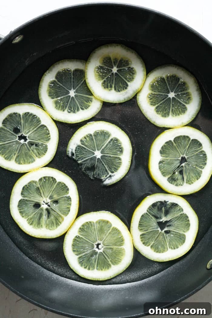 Thinly sliced lemons simmering gently in simple syrup within a wide skillet, becoming translucent.