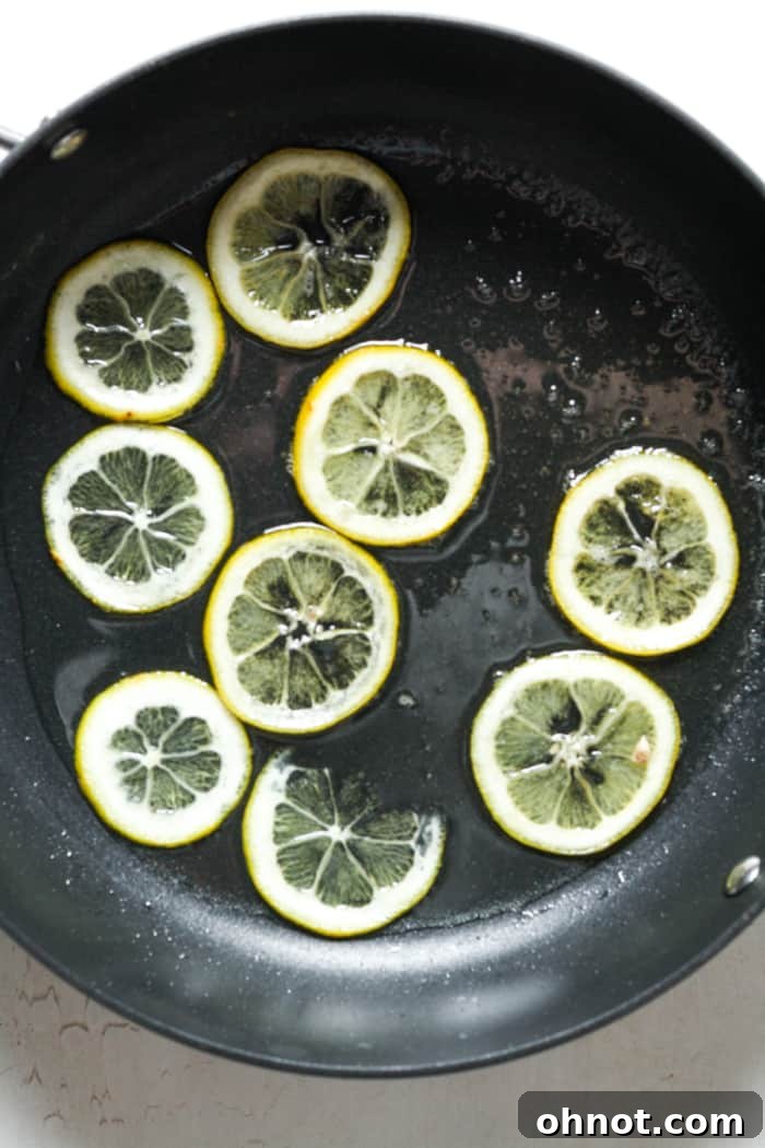 Freshly candied lemon slices cooling on a parchment-lined pan, glistening with residual syrup.