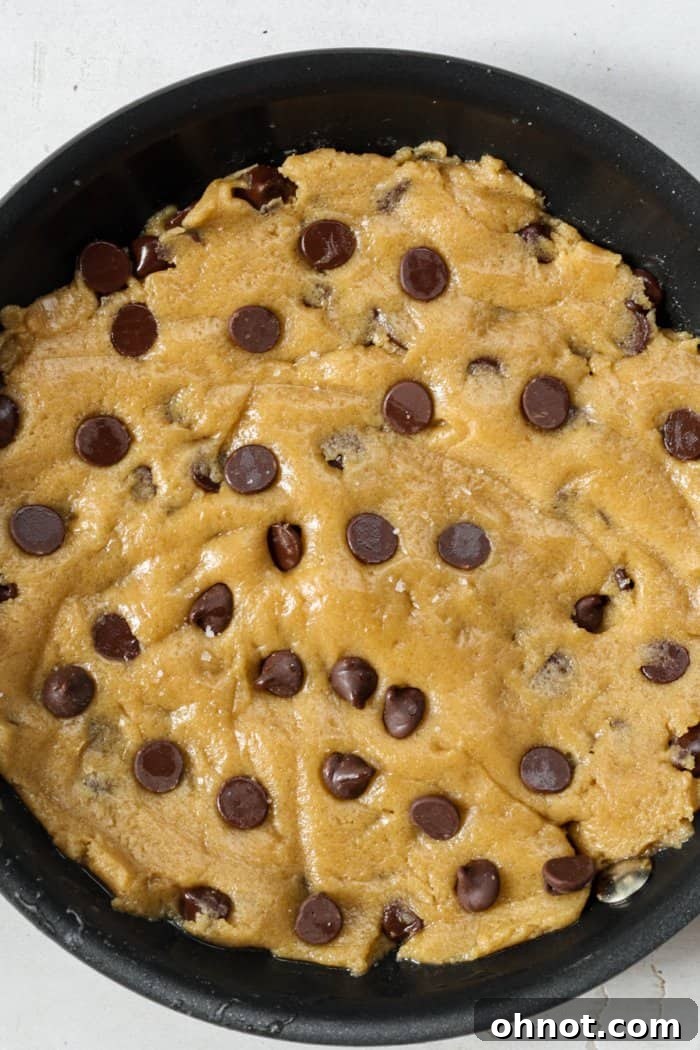 Raw cookie dough spread evenly in a mini skillet, ready for the oven.