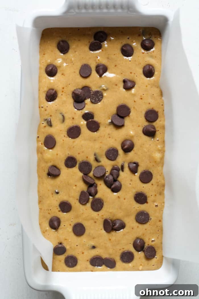 Raw banana bread batter with chocolate chips poured into a lined loaf pan.