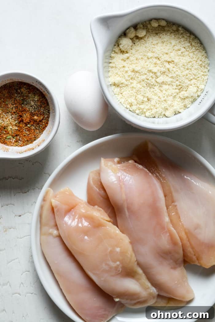 Bowls of raw chicken strips and a selection of seasonings on a counter.