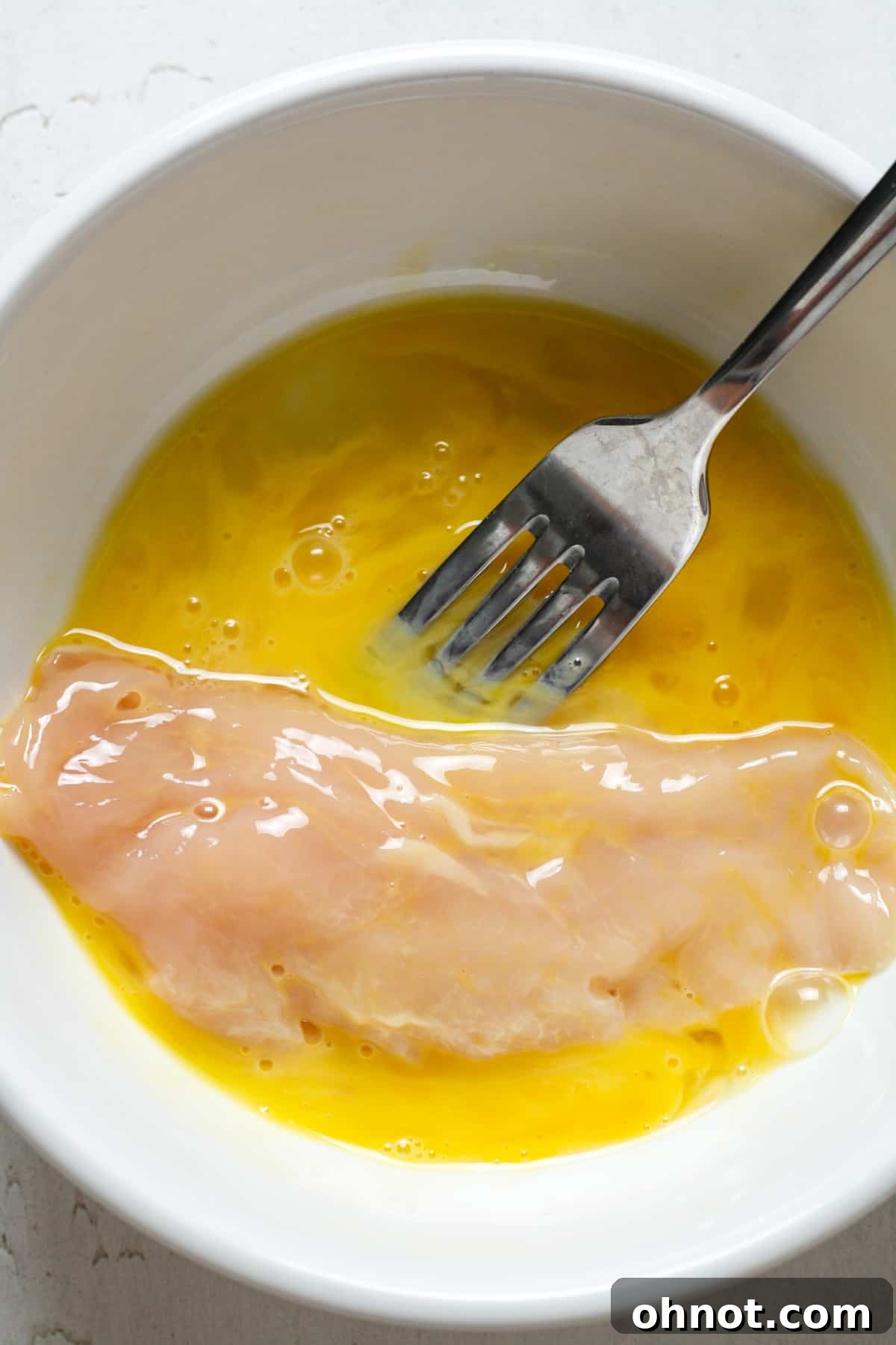 Chicken tender being dipped into egg wash.