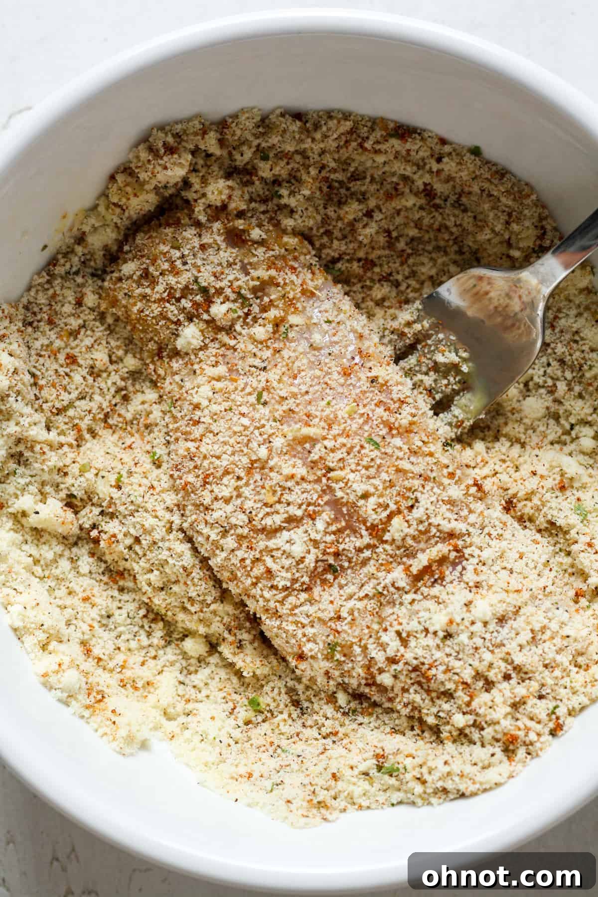 Chicken tender being coated in dry almond flour mixture.