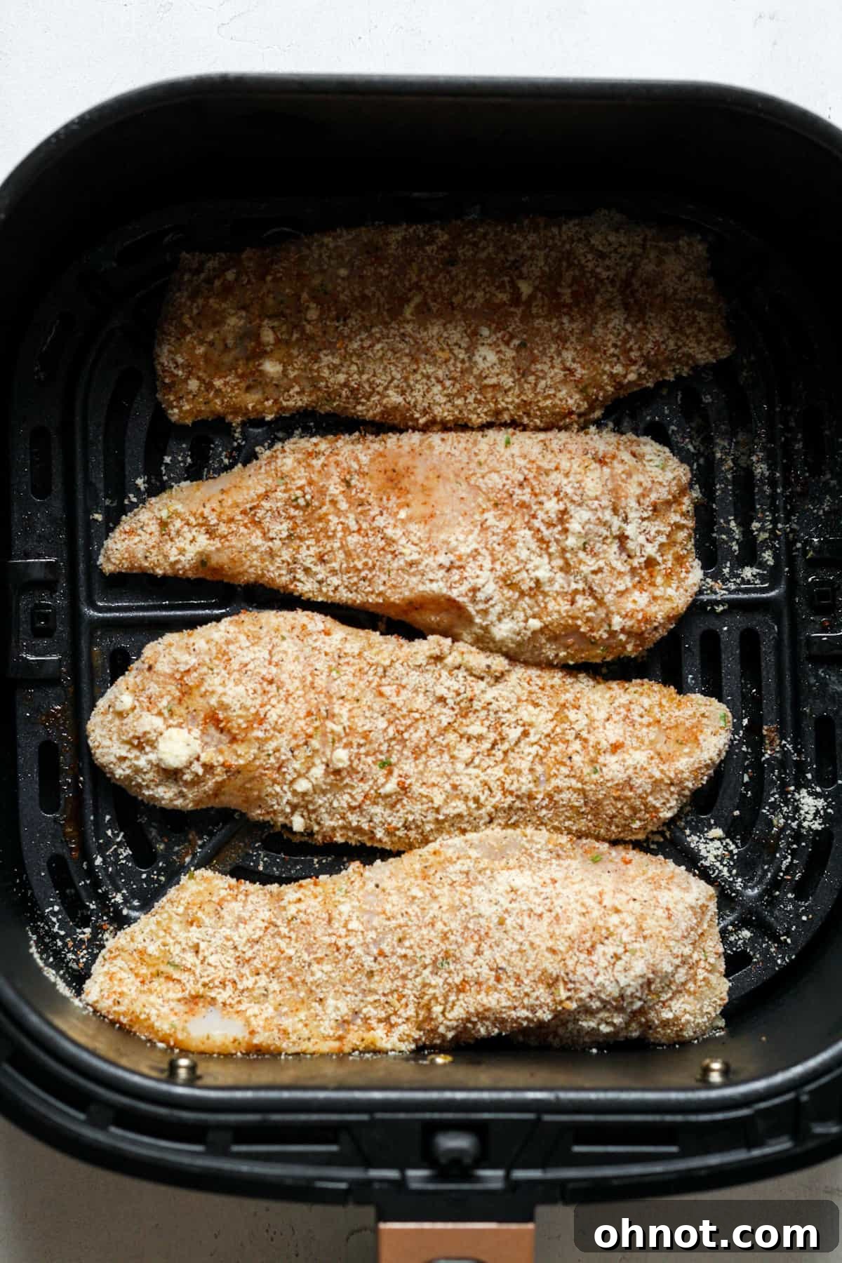 Coated chicken tenders arranged in an air fryer basket.