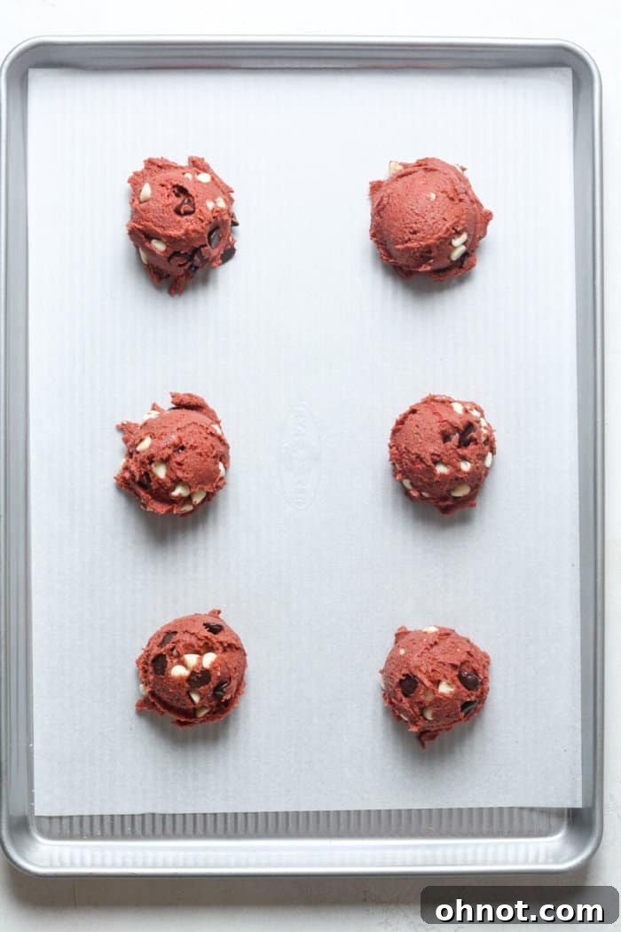 Scooped red cookie dough balls evenly spaced on a baking sheet lined with parchment paper.