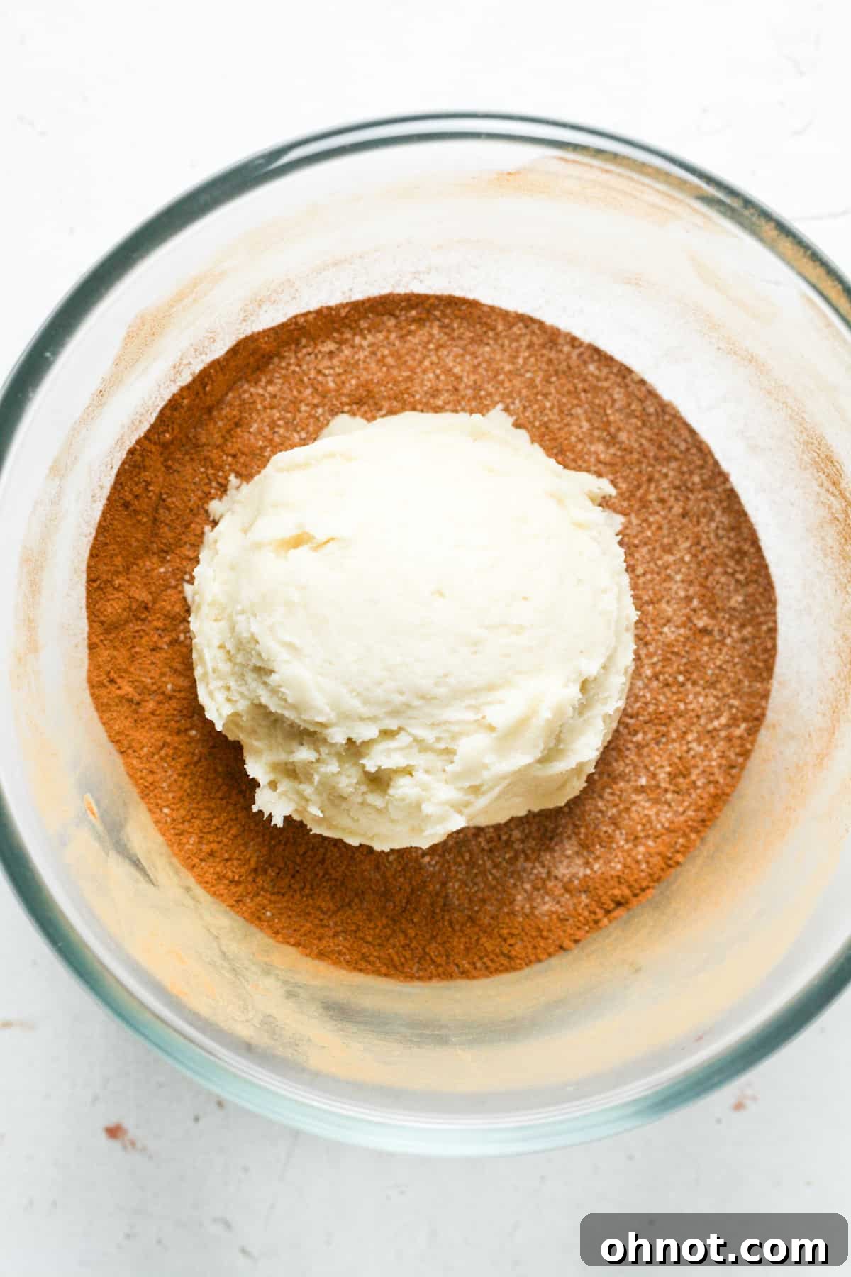 Cookie dough ball being rolled in a bowl of cinnamon sugar mixture.