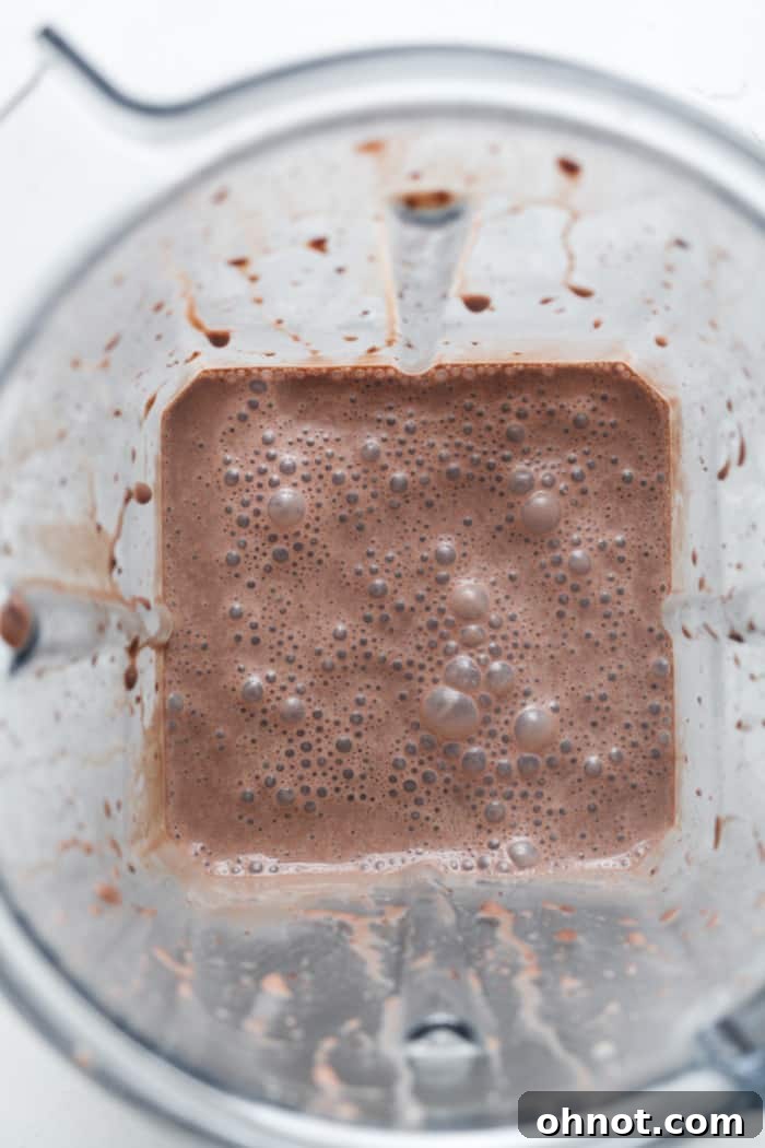 A high-speed blender actively mixing a chocolate vegan milkshake to a smooth consistency.
