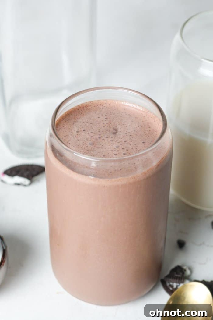 Two tall glasses filled with freshly made vegan chocolate milkshakes, topped with generous swirls of vegan whipped cream and chocolate shavings.