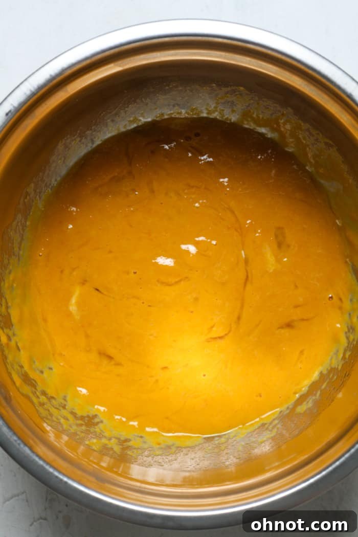 Vibrant orange batter, a blend of eggs, pumpkin puree, and vanilla extract, sits in a mixing bowl.