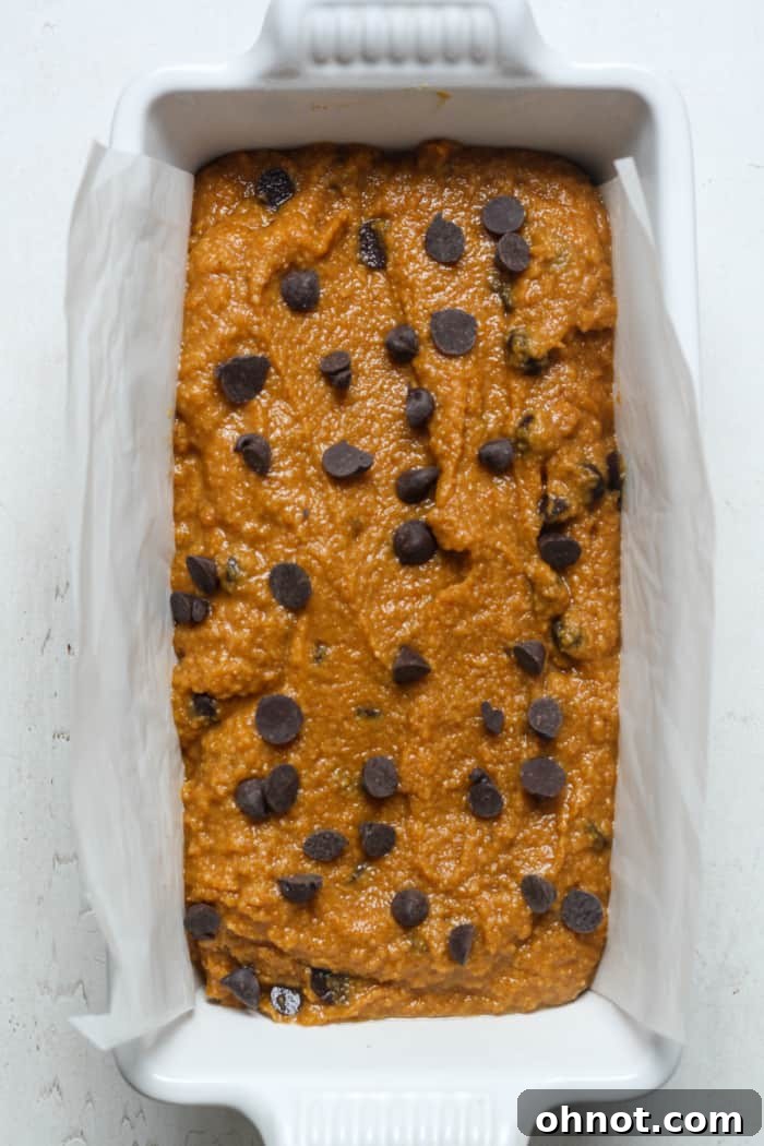 A loaf pan, perfectly lined with parchment paper, now filled with the pumpkin bread batter, ready for the oven.