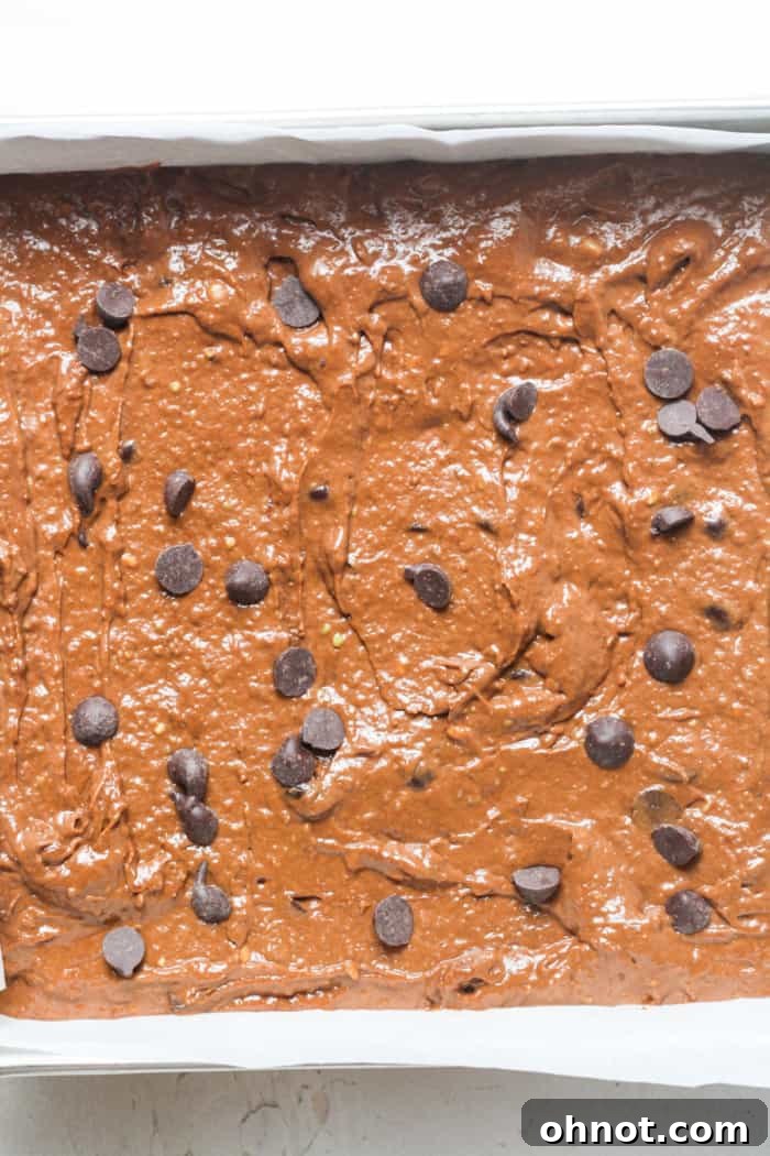 Unbaked vegan brownie batter spread in a parchment-lined pan.