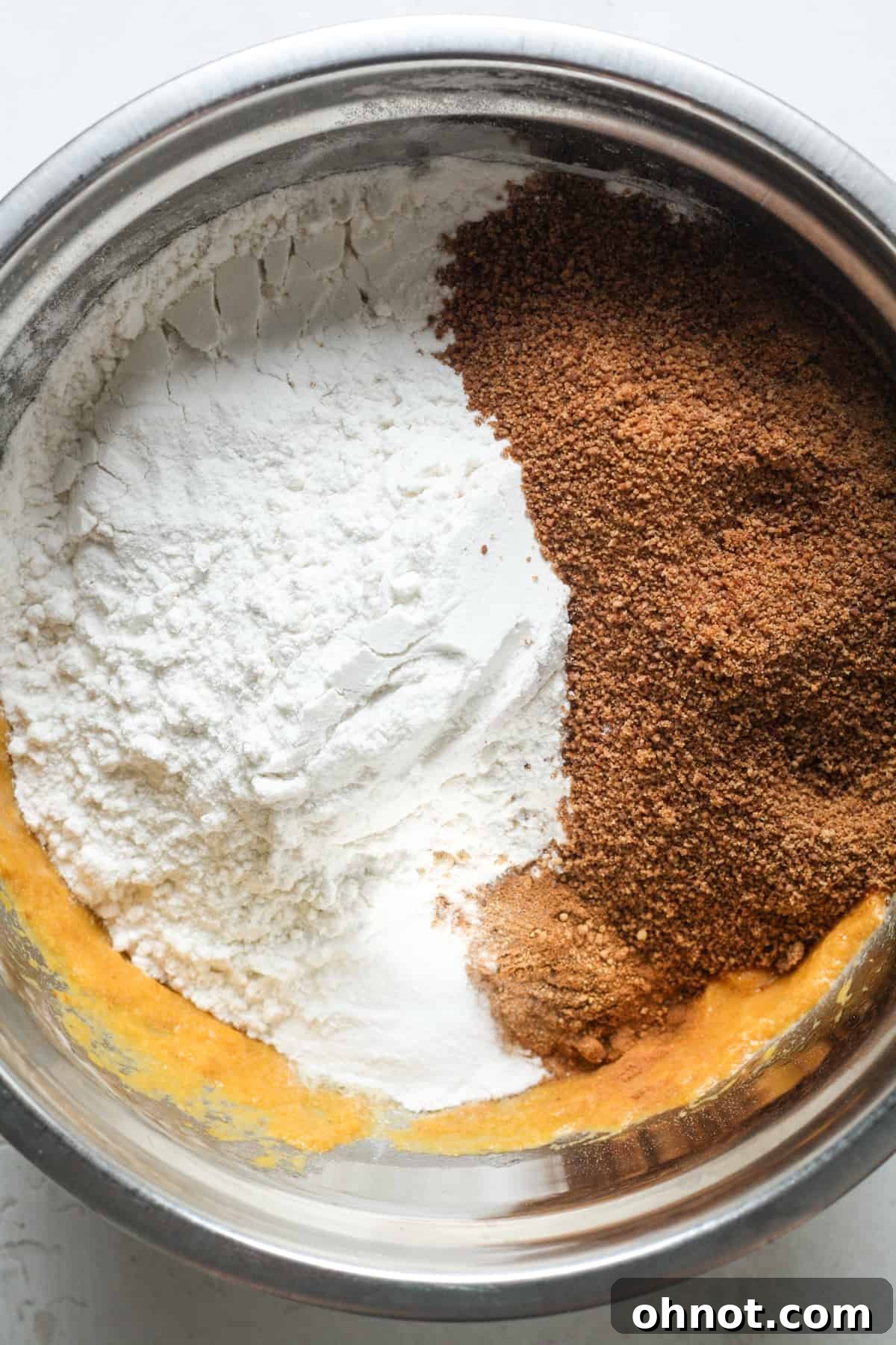 Dry ingredients like flour and coconut sugar added to the wet pumpkin mixture in a bowl.