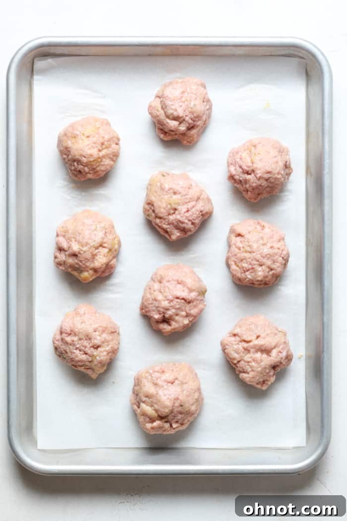 Raw, perfectly shaped turkey meatballs arranged on a parchment-lined baking pan.
