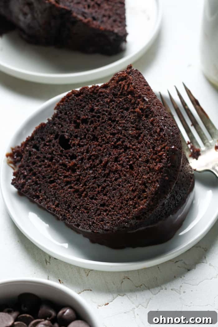 A perfect slice of moist chocolate brownie cake, topped with glaze, resting on a white plate.