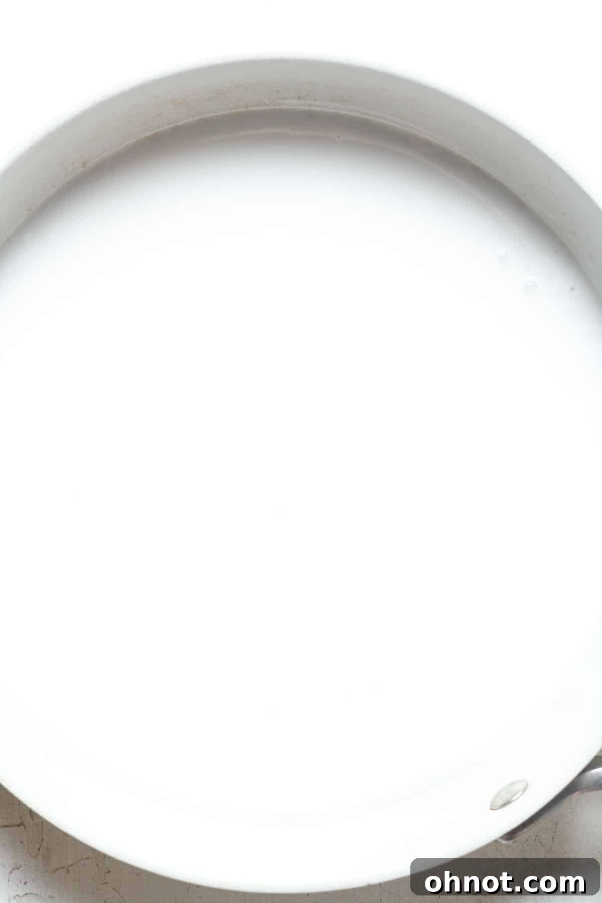 Coconut milk heating gently in a small saucepan on the stovetop.