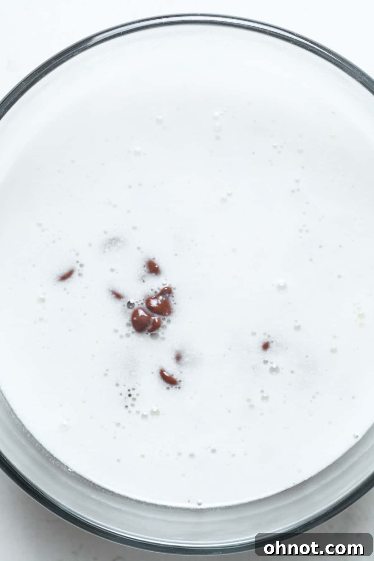 Hot coconut milk being poured over chocolate chips in a bowl to create a glaze.