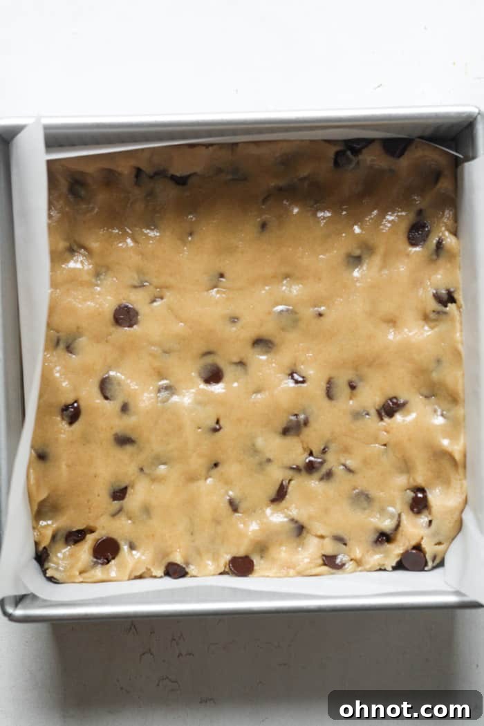 Raw cookie bars pressed into a parchment-lined pan.
