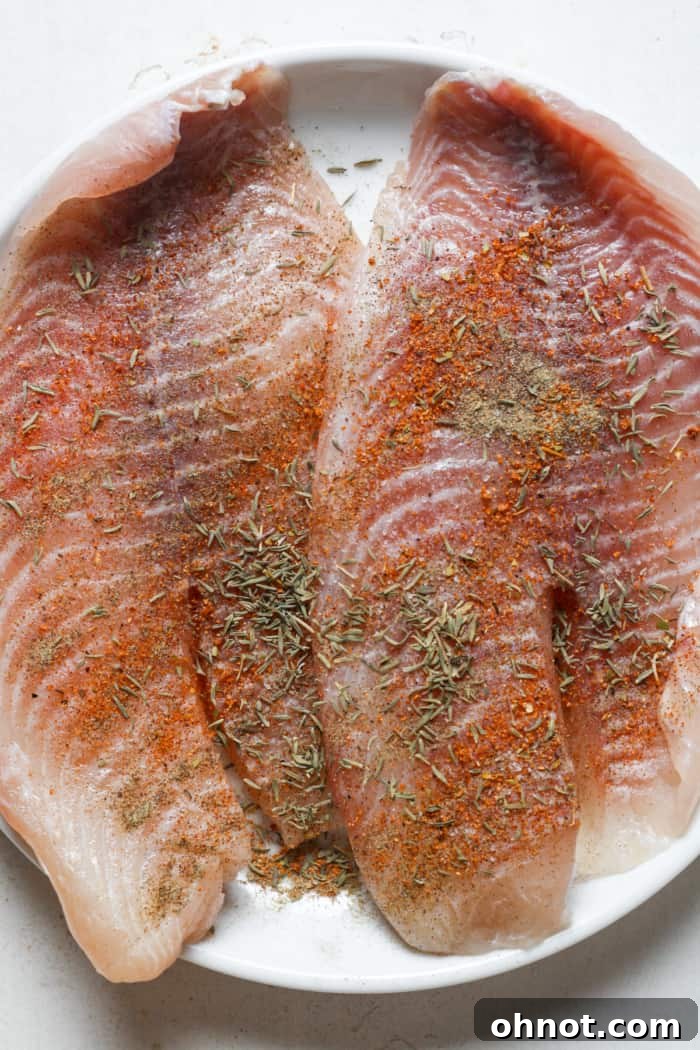 Fresh tilapia fillets seasoned with herbs and spices on a plate.