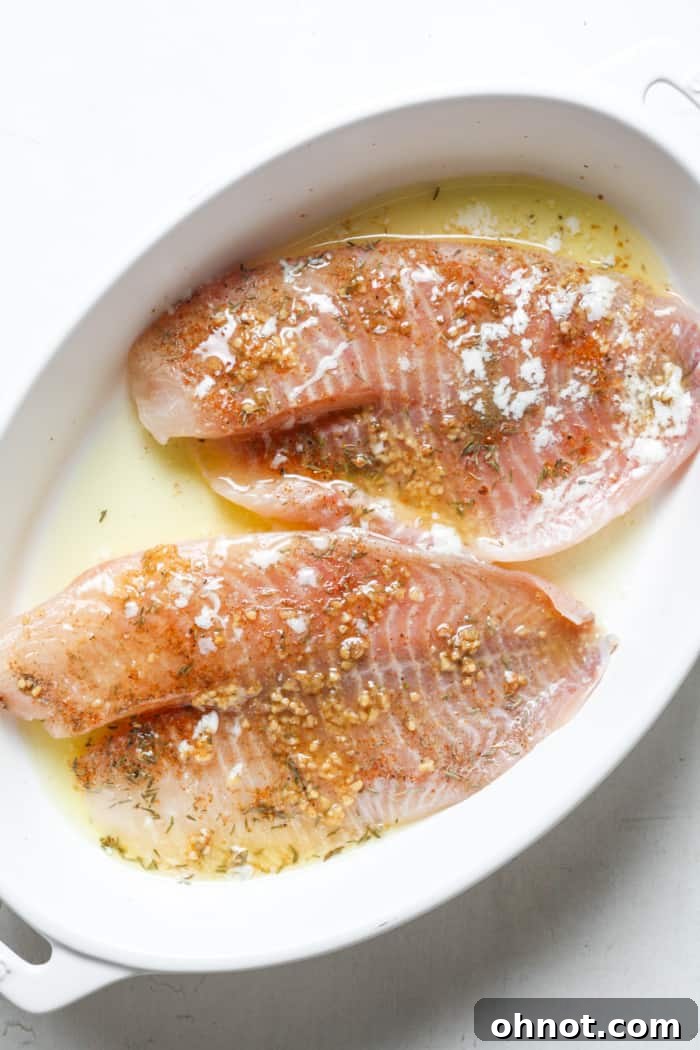 Tilapia fillets arranged in a baking dish with lemon, garlic, and butter poured over.
