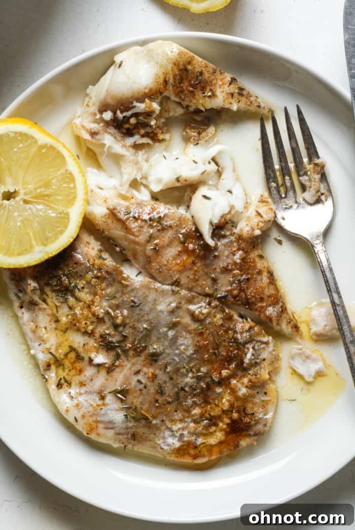 Plate of lemon garlic butter baked tilapia, garnished with fresh lemon.