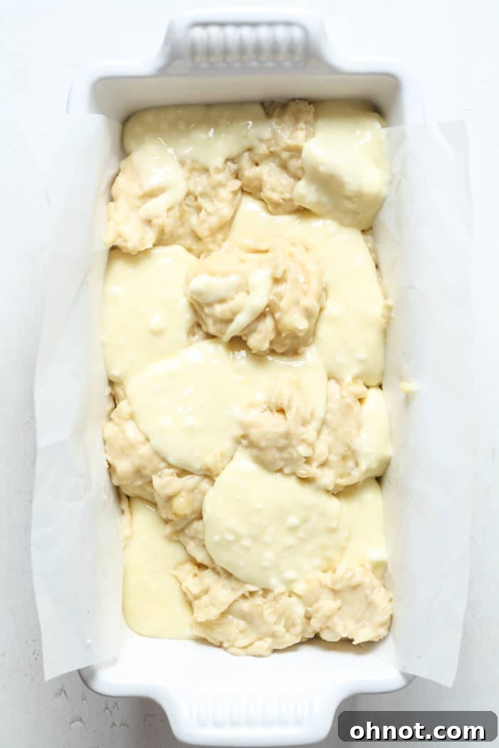 Alternating dollops of banana bread batter and cream cheese filling in a loaf pan.