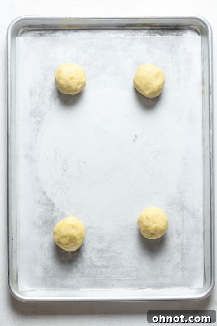 Four perfectly spaced cookie dough balls resting on a parchment-lined baking sheet, ready for the oven.