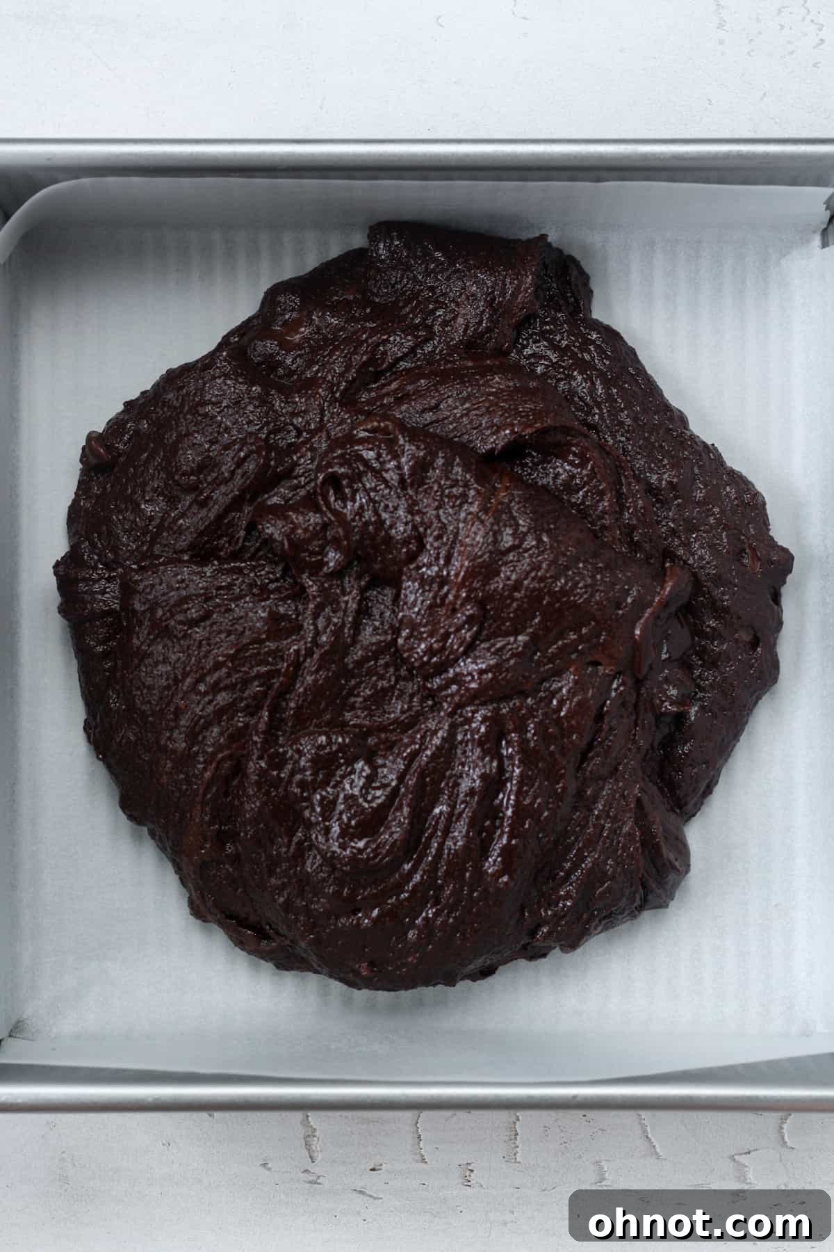The thick vegan brownie batter being spread into a parchment-lined square baking pan.
