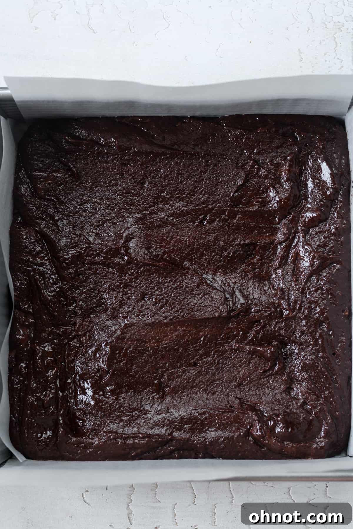 A square baking pan filled with raw vegan brownie batter, smoothed into an even layer, ready for the oven.