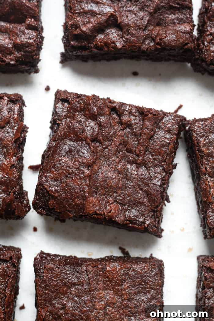 Close-up of a rich, fudgy vegan brownie with a shiny, crackly top, showcasing its perfect texture.