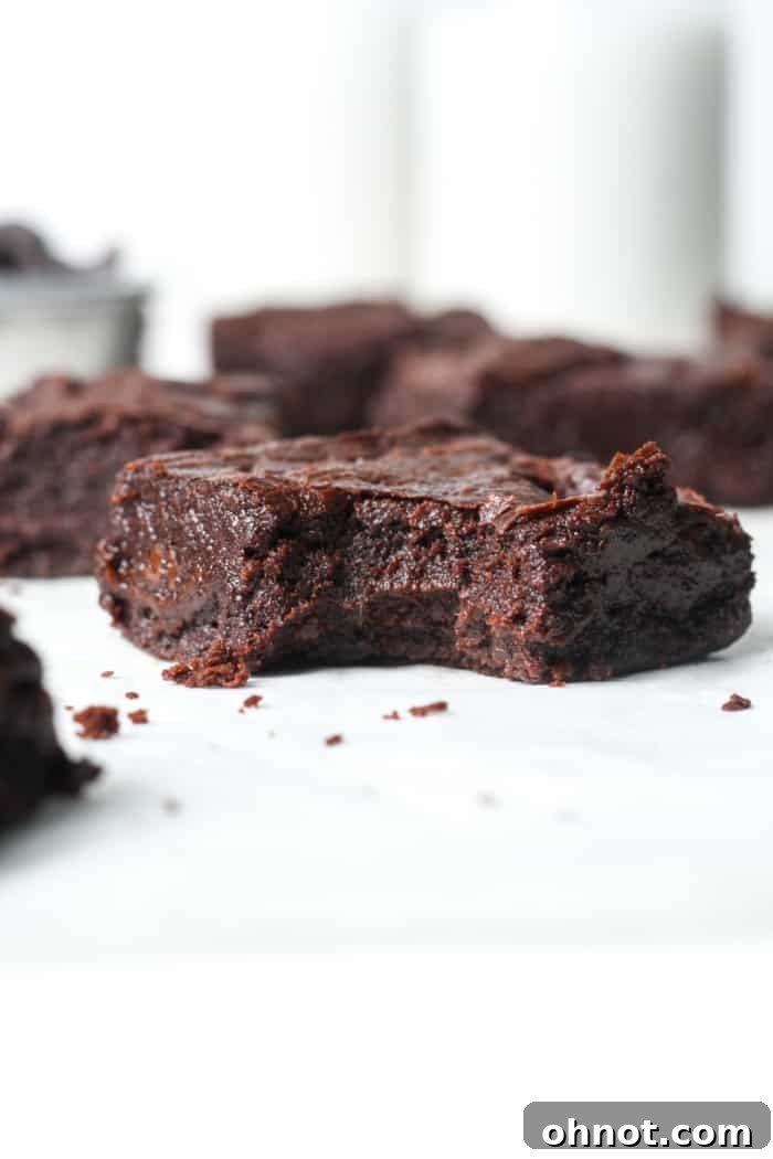 A hand holding a bite-sized piece of a vegan chocolate brownie, showing its moist interior.