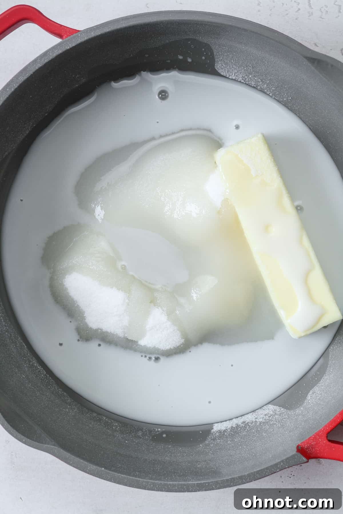 A skillet on a stovetop with vegan butter, vegan milk, and granulated sugar, beginning to melt and combine over low heat.