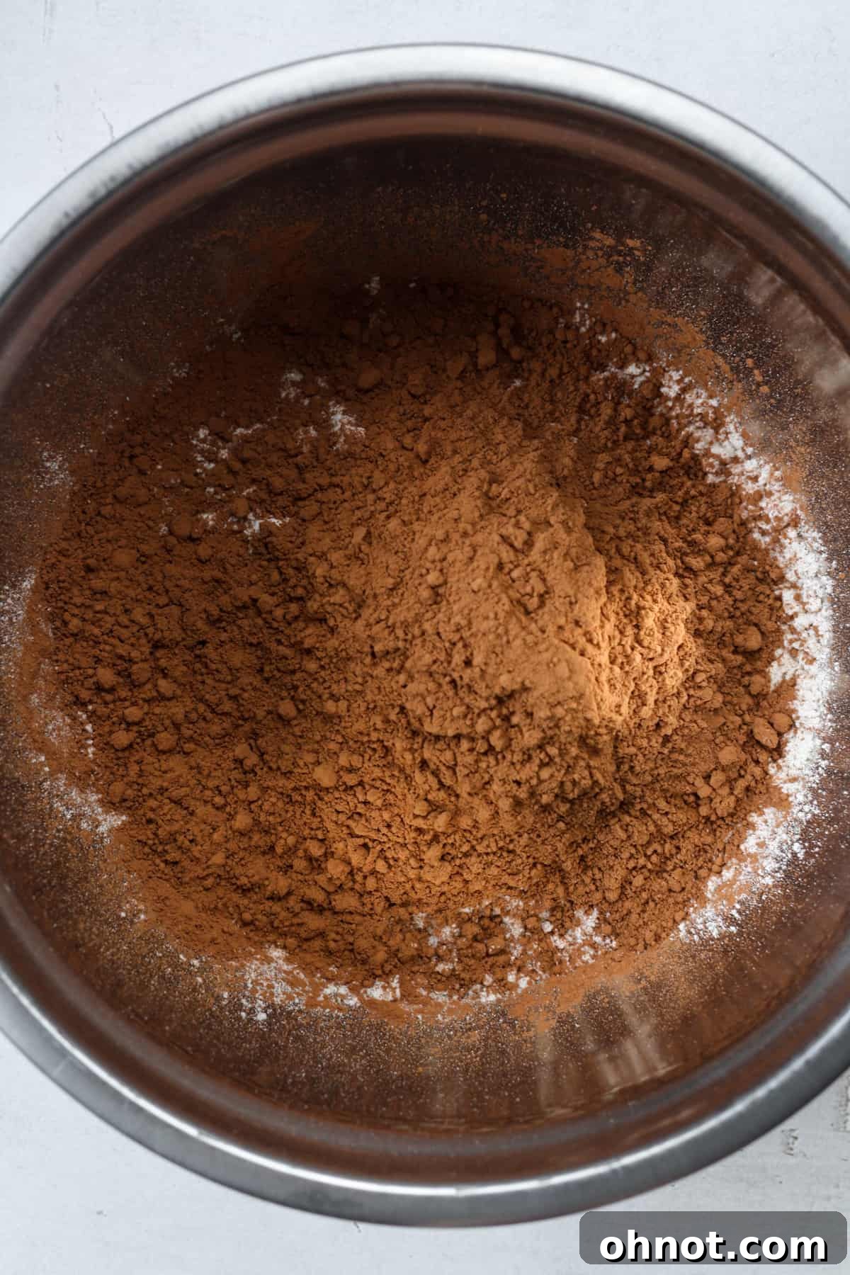 Dark cocoa powder being added to flour in a mixing bowl.
