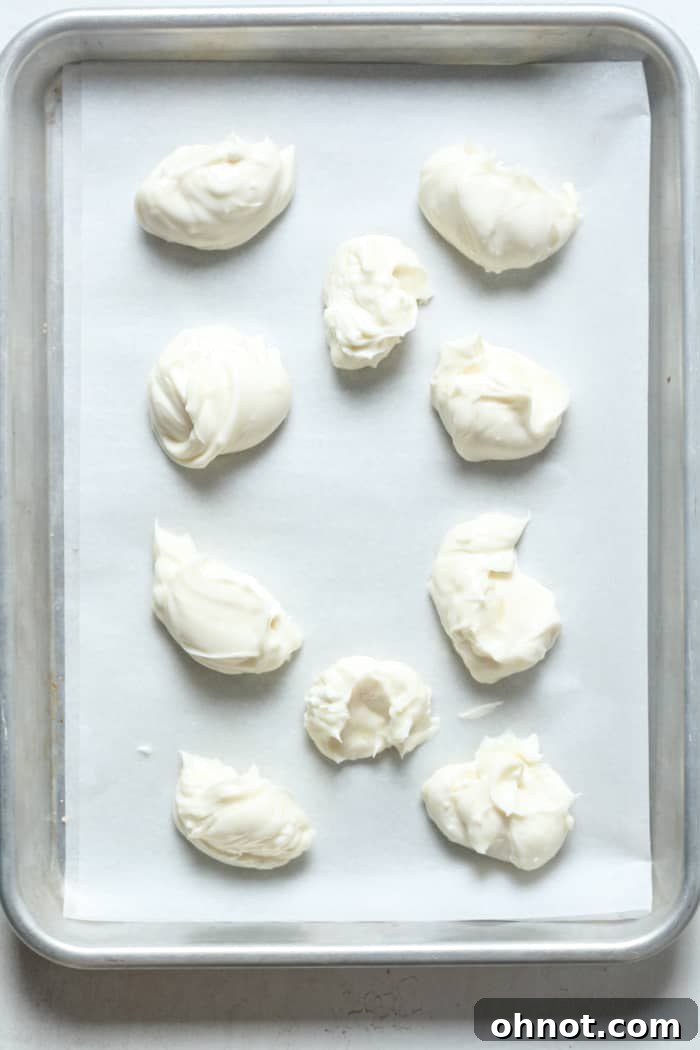 Small, uniform cream cheese balls arranged on a parchment-lined baking sheet.