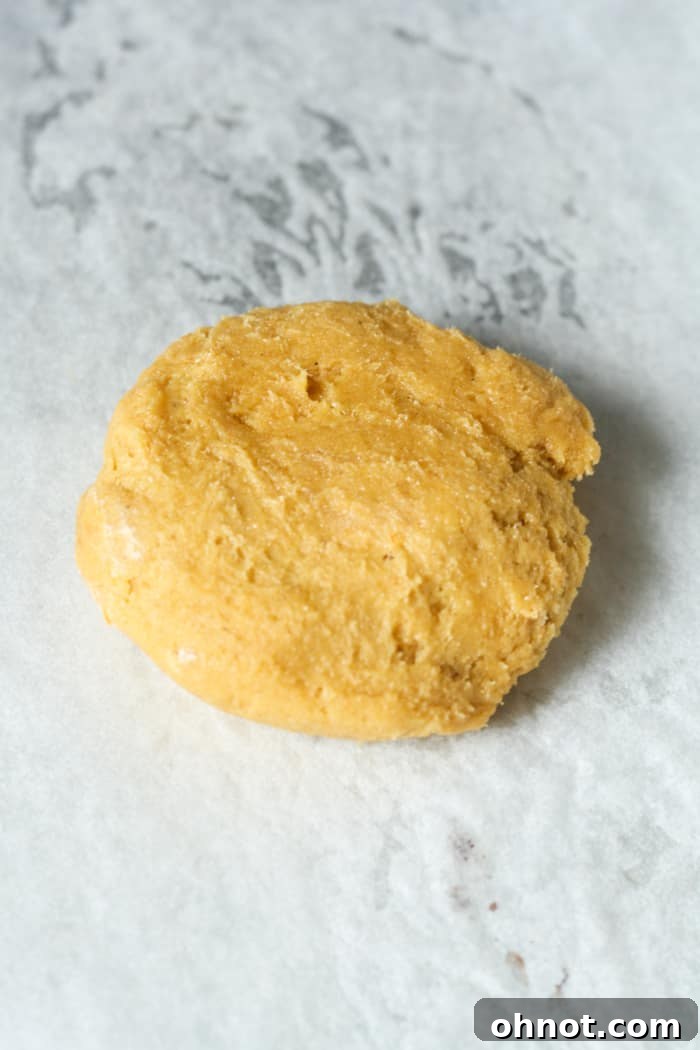 Flattened orange pumpkin cookie dough disc on a baking sheet.