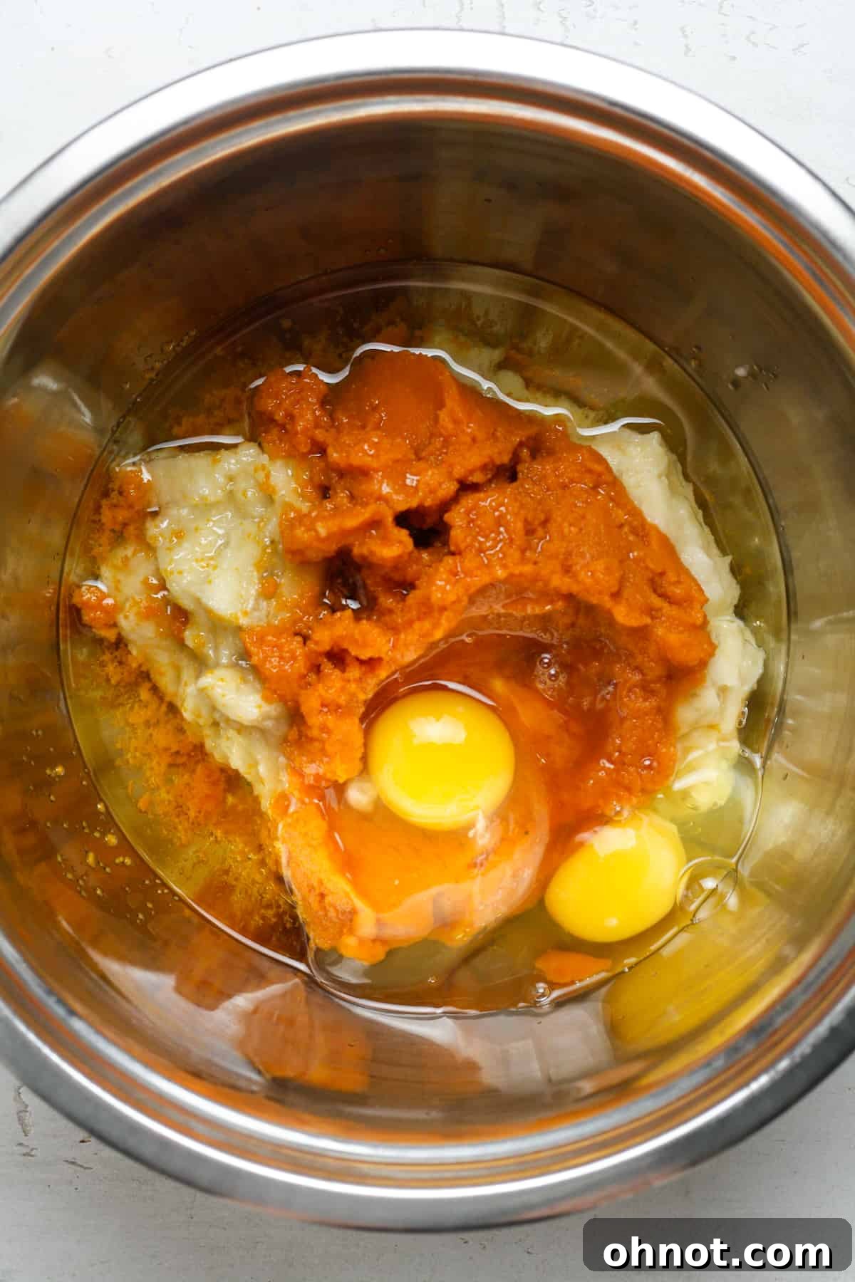 Wet ingredients in a mixing bowl, featuring orange pumpkin purée and whisked eggs.
