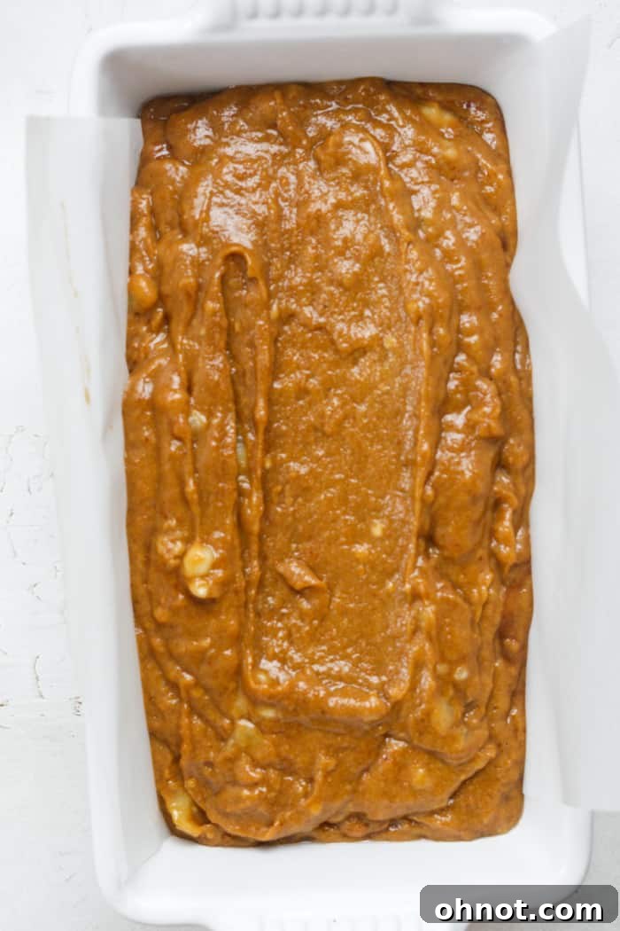 Raw pumpkin banana bread batter perfectly smoothed in a parchment-lined loaf pan, ready for baking.