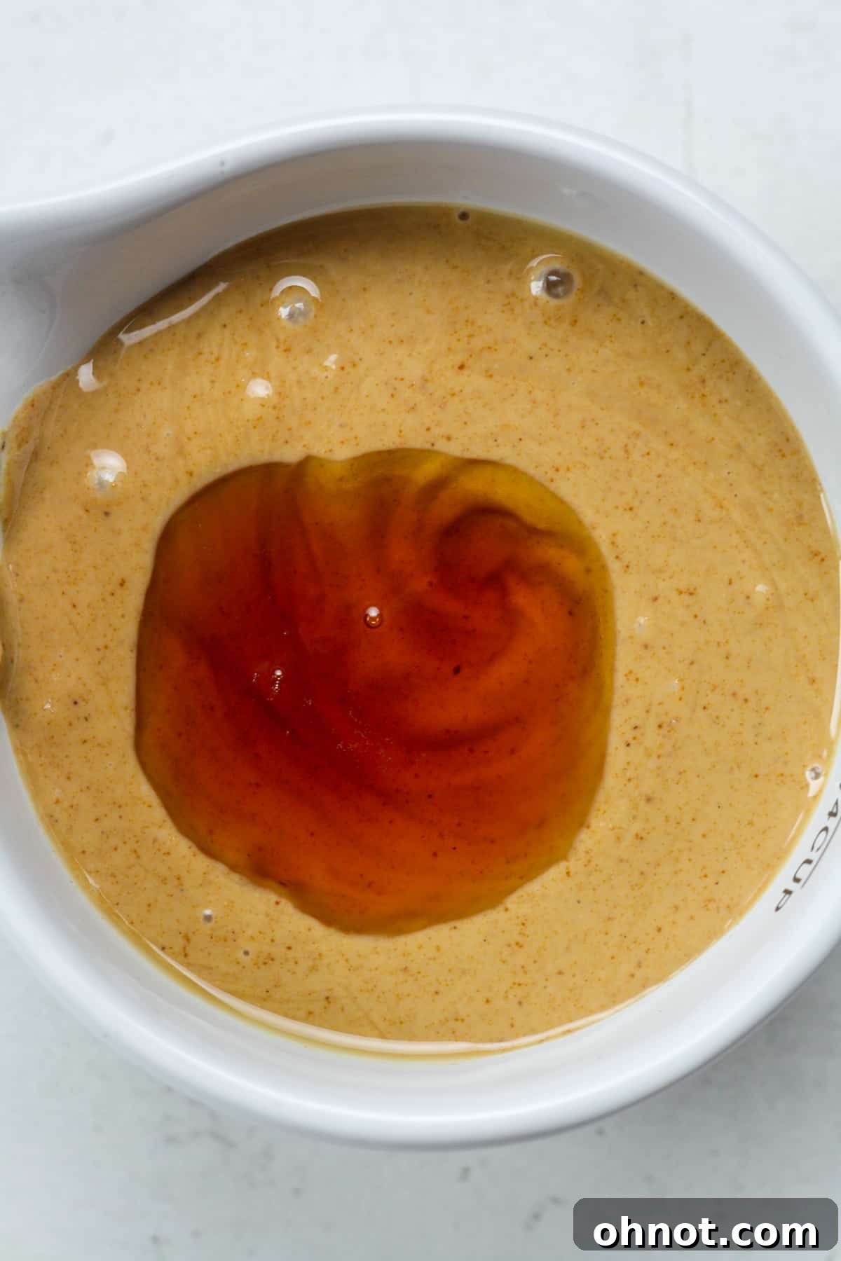 Maple syrup being added to peanut butter in a bowl.