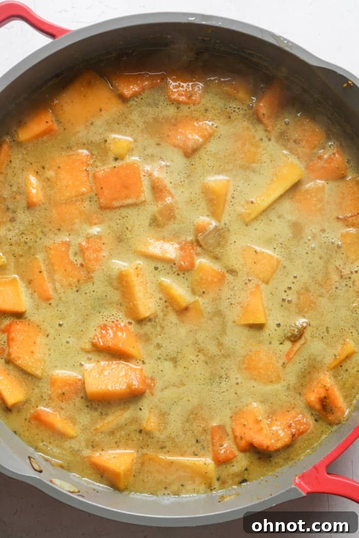 Butternut squash simmering in a creamy curry sauce in a covered skillet.